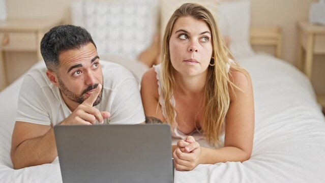 Man and woman couple lying on bed together using laptop looking around at bedroom