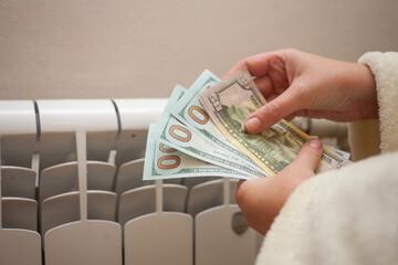 Concept cost of heat energy. A woman holds money in her hands near a heating radiator.