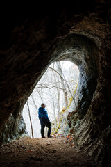 The boy stands in the center of the cave vault, view from the inside of the underground cave, oval entrance to the grotto, natural object, karst cavity in the mountain.