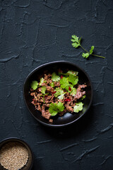 Spicy carpaccio salad with green coriander, lime, sesame seeds and red hot chili pepper in a black bowl.