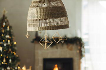 Rustic scandinavian straw decoration hanging on background of festive golden lights bokeh in modern farmhouse living room. Decorating home with christmas straw spiders. Holiday traditions