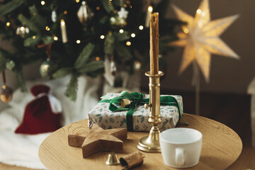 Stylish wooden table with christmas gift, candle, cup and star on background of christmas tree and...