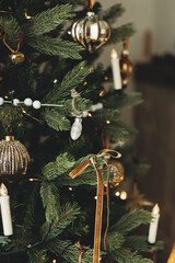 Stylish decorated christmas tree with vintage baubles, ribbons, candles and golden lights....