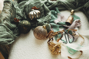 Fototapeta na wymiar Stylish christmas vintage baubles, ribbons, brass bells and scissors on cozy white chair. Christmas ornaments aesthetics flat lay. Decorating for christmas holidays. Merry Christmas