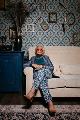 Fashionable senior woman in trendy and luxury wear sitting on comfortable couch at retro house