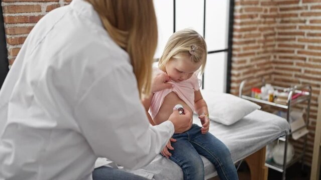 Caring pediatrician in clinic examining adorable kid patient's chest using stethoscope, ensuring hearty breath during medical exam in cozy indoor healthcare center