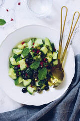 Healthy salad with fresh vegetables - cucumber, black olives, mint and red hot chilli pepper on a white plate.