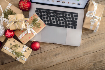 Open laptop with Christmas gift boxes and balls on a wooden table top view. Holiday sale, shopping concept