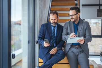 Two happy business colleagues at meeting in modern office interior. Successful mature boss in a conversation with young employee in boardroom. Marketing team of two businessmen discussing 