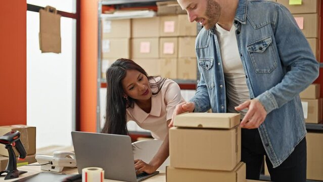 Two workers man and woman using laptop putting packages on table at office