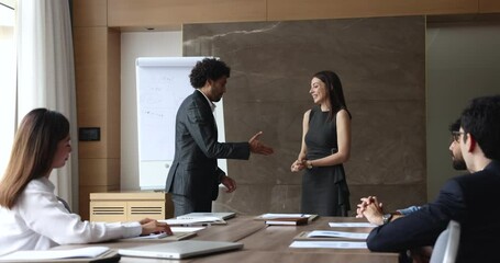 Male leader praising happy female colleague at group meeting. Diverse staff applauding, supporting new worker, congratulating with professional achievement, promotion, shake hands express recognition