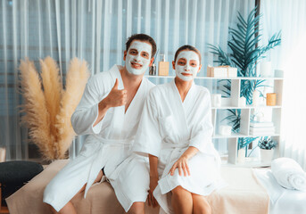 Blissful couple in bathrobe with facial cream mask enjoying serene ambiance of spa salon resort or...