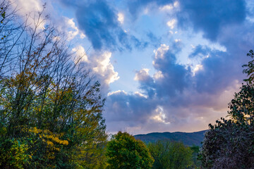 Spectacular autumn sunset over trees and mountains. Colorful, dense clouds fill the sky on a chilly day, capturing the essence of fall and weather