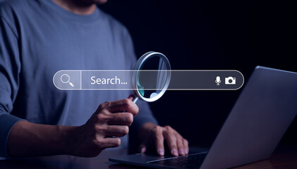 Search engine technology concept, Businessman holding magnifying glass and using laptop computer to Searching for internet information with web browser. Job search bar on website, Research online, - obrazy, fototapety, plakaty
