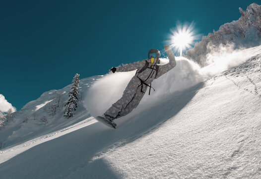 Fast professional snowboarder rides in cloud of powder snow over offpiste ski slope. Backcountry extreme sports