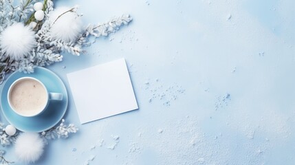 A serene winter composition featuring a steaming mug, wintry branches, fluffy ornaments, and a white card on a frosted blue surface.