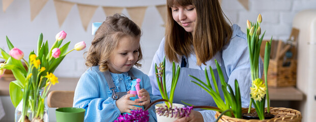 Happy mother and daughter doing home gardening together in the kitchen, taking care about flowers,...