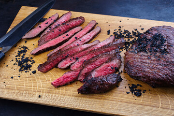 Traditional barbecue wagyu gourmet flank steak sliced with black salt served as close-up on a wooden design cutting board with a Japanese santoku knife