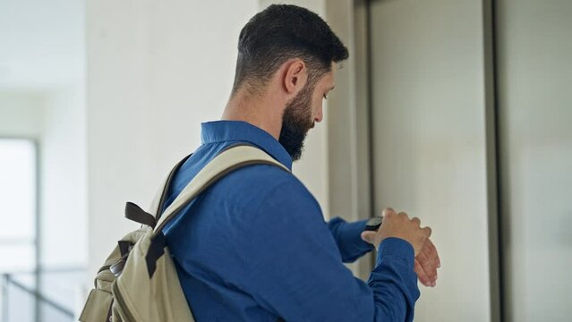 Young hispanic man business worker looking watch getting in elevator at the office