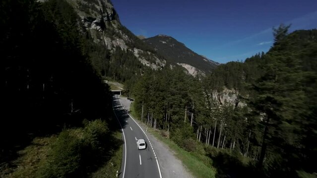 areal footage of white car going uphill in mountains, epic view of alps 