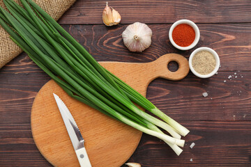 Board with fresh green onion and spices on wooden background