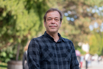 Portrait of a confident man of 45-50 years old on a neutral blurred background of a city park.