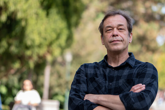 Portrait Of An Older And Confident 50-55 Year Old Man Wearing A Shirt On A Neutral Urban Background, Looking Into The Camera, Space For Text, Copy Space.