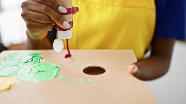 African american woman artist pouring color on palette at art studio