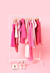 Rack with pink clothes and shoes on color background