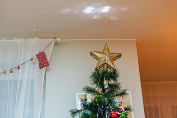 Beautiful interior view of room adorned with Christmas tree topped with gold star and electrical projection that scatters snowflakes onto ceiling. Sweden.