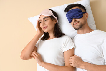 Young couple in sleeping masks with pillow on beige background