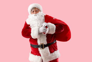 Fototapeta na wymiar Santa Claus with bag full of Christmas gifts on pink background