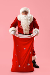Santa Claus with bag full of Christmas gifts on pink background