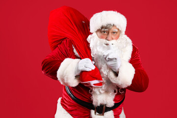 Santa Claus with bag full of Christmas gifts showing silent gesture on red background