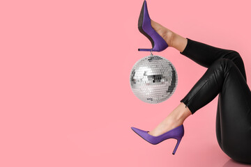 Female legs in stylish high heels with disco ball on pink background
