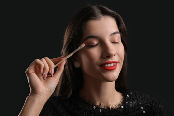 Obraz premium Beautiful young woman with brush applying eyeshadows on black background
