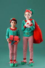 Cute little children in elves costumes with Santa bag full of gifts on green background