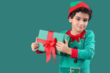 Cute little boy in elf costume with Christmas gift box on green background