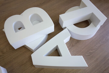 White PVC plastic letters lie on a wooden table in the workshop. Assemble a logo for an information...