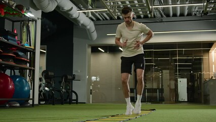 Caucasian sportsman man footballer soccer player training in sports gym exercise with ladder sport equipment workout cardio exercising jumping prepare for football match male athlete in fitness club - Powered by Adobe