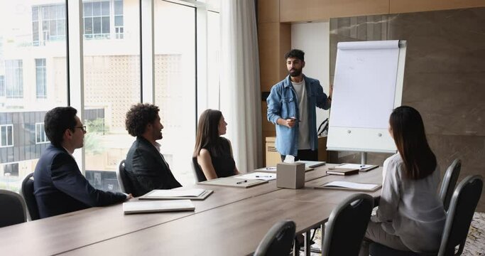 Young trainer writing on flip chart during presentation for corporate clients or staff members take part in seminar or business training in company conference room. Education, coaching, workshop event
