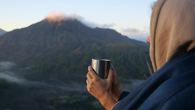 Close-up of woman wrapped in blanket holding hot coffee, enjoying view of mountains Cinematic video of mountains with peaks in clouds, camping traveler Spend weekend in camping, meet dawn in mountains