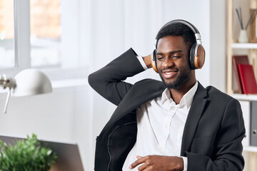 An African-American man sits at his desk in front of his laptop, wearing headphones and chatting on a video call, listening to music. The concept of student business training and online work.