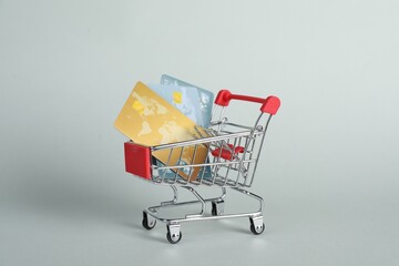 Small metal shopping cart with credit cards on light background