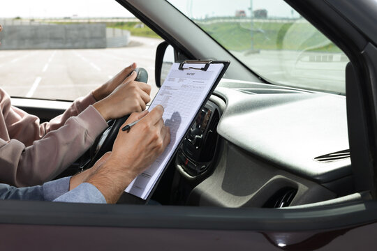 Driving school. Student passing driving test with examiner in car at parking lot, closeup