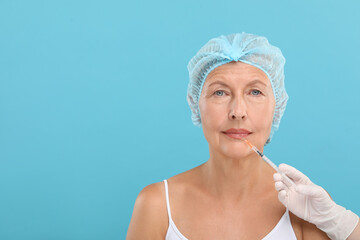 Doctor giving lips injection to senior woman on light blue background, space for text. Cosmetic surgery