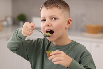 Cute boy eating tasty fresh kiwi indoors, closeup