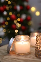 Burning candles on wooden table in room decorated for Christmas