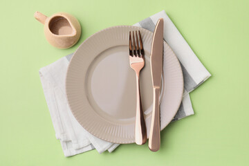 Clean plate with cutlery, saucepan and napkin on light green background, flat lay