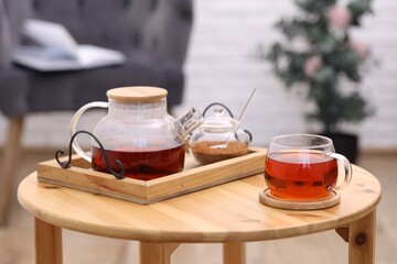 Teapot, cup of aromatic tea and brown sugar on wooden table indoors